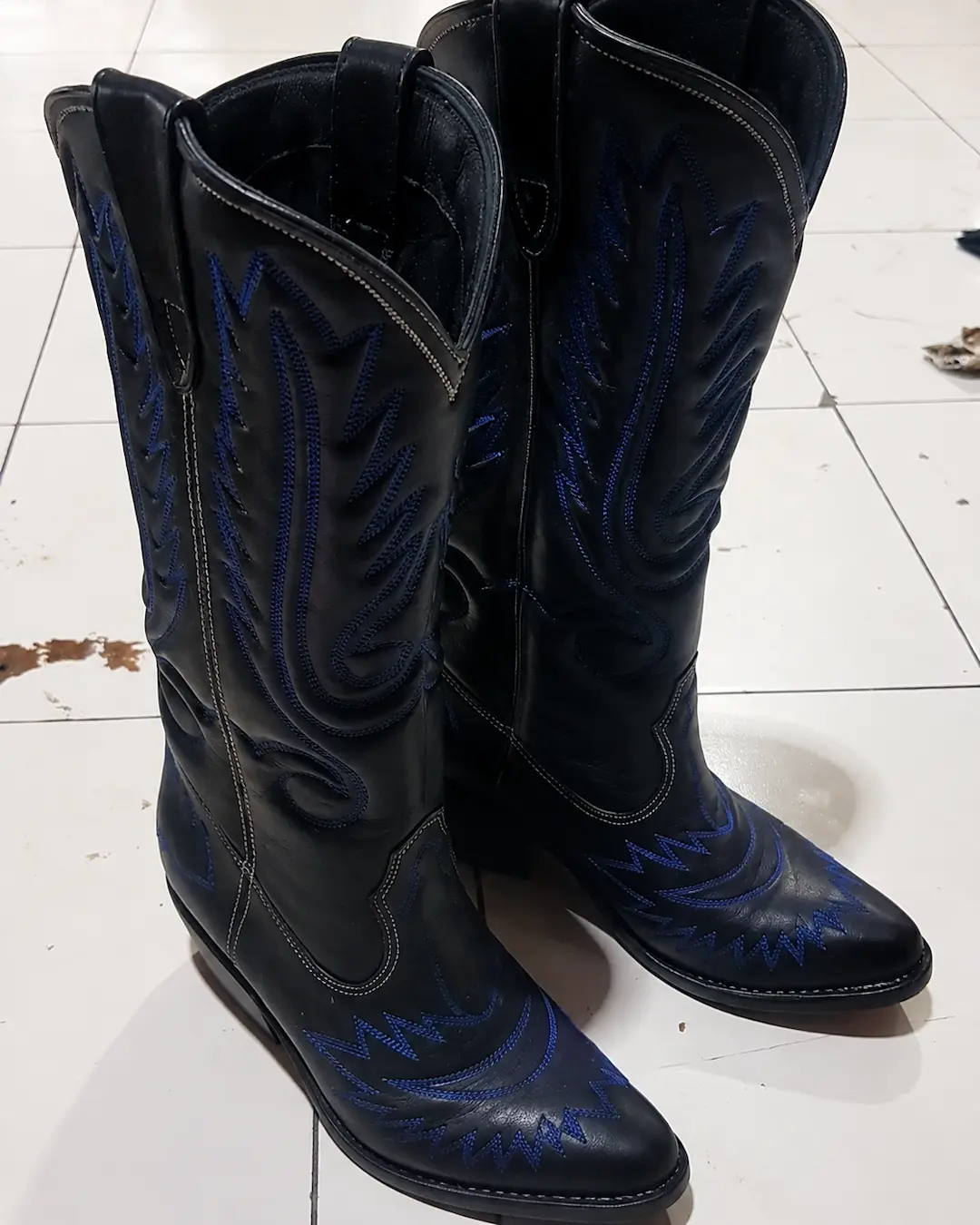 Detail close-up bordir biru pada cowboy boots hitam.